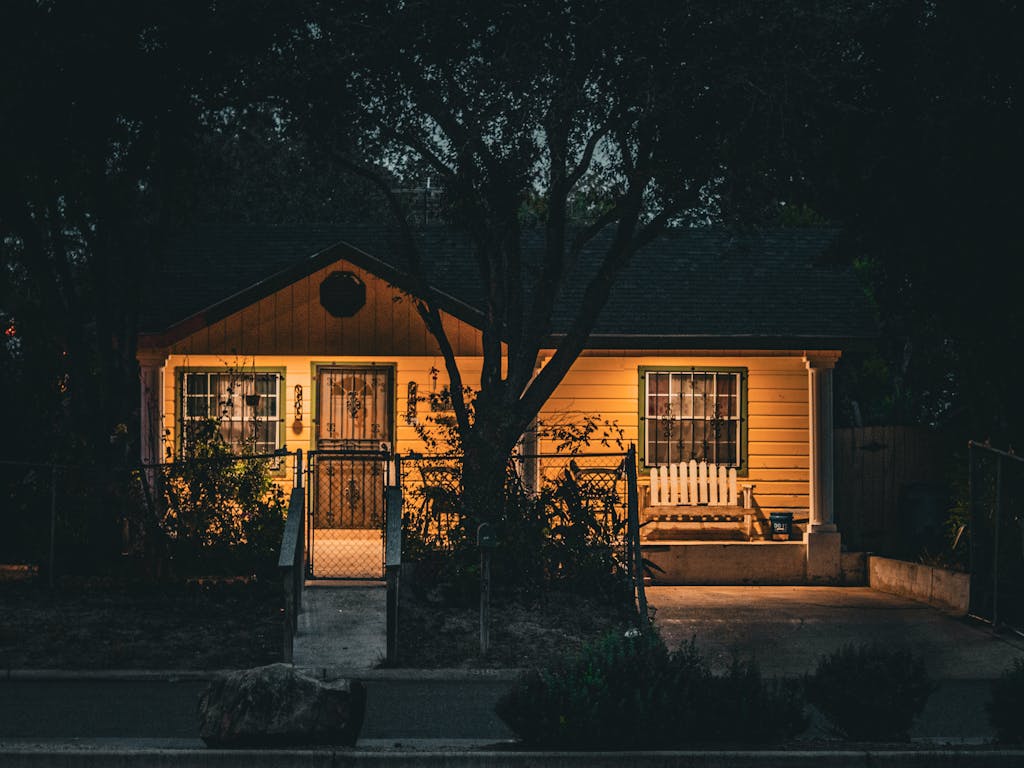 A cozy yellow house warmly lit amidst trees in Texas during nighttime, exuding homely charm.